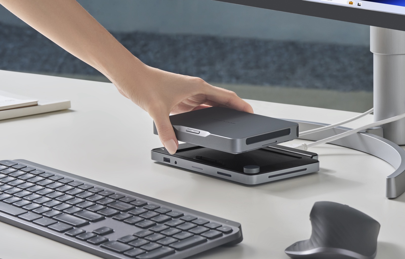 A hand lifting the Mind off its dock at a home desk